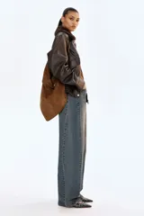 Jean de cinco bolsillos en denim de algodón rígido, color azul oscuro con efecto desgastado. Modelo de cintura clásica con cierre y botón, corte holgado y piernas anchas tipo barrel con costuras laterales marcadas.