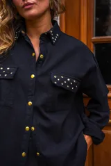 Camisa de denim negra con botones metálicos dorados y bolsillos con tachas doradas. De corte amplio.