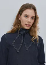 Camisa azul oscuro de denim con cuello alto y detalle de bufanda integrada en el mismo tejido.