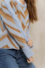 Sweater de punto jacquard con diseño de chevron en tonos celeste y marrón. Presenta cuello redondo, corte holgado y mangas largas con hombros abullonados.