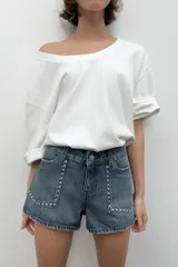 Shorts de jean tiro medio con bolsillos delanteros de plastrón decorados con tachas metálicas. Presenta cierre frontal con cremallera y botón metálico.