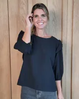 Blusa de algodón color negro, con diseño de volados en los hombros y mangas tres cuartos con puños elásticos.