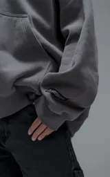 Hoodie oversize de corte crop, color gris oscuro, confeccionado en frisa de algodón. Presenta capucha forrada, bolsillo tipo canguro frontal y puños elásticos.