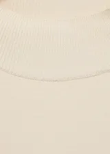 Jersey de punto fino color crema con cuello perkins y manga larga. Presenta un detalle de botones metálicos decorativos en uno de los hombros y un diseño de corte recto.