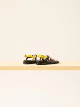 Sandalia baja de cuero vacuno con tiras cruzadas y aplique decorativo. Tiene hebilla en el talón y empeine para regular el calce.