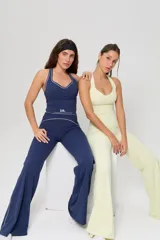 Conjunto deportivo compuesto por una musculosa de cuello halter con vivos en contraste y un pantalón de corte recto con cintura alta y detalles de costuras decorativas. Ambas piezas presentan el logo de la marca estampado.