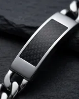 Pulsera de eslabones tipo cubana fabricada en acero inoxidable, con una placa central decorada con un inserto de fibra de carbono.