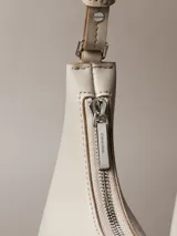 Cartera de hombro Calvin Klein de diseño estructurado en color beige, con cierre de cremallera superior, correa ajustable y detalle del logo de la marca grabado en la parte frontal.