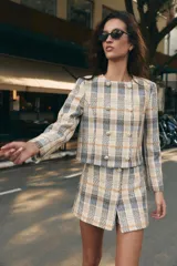 Falda pantalón de tiro alto confeccionada en tejido de tweed con estampado a cuadros en tonos beige, azul y negro. Presenta detalles de falsos botones y cierre lateral con cremallera oculta.