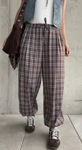 Pantalón babucha de corte holgado, con estampa de cuadros en tonos marrón y celeste, cintura elástica con cordón ajustable y puños fruncidos en los tobillos.
