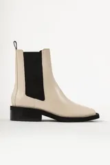 Bota tipo Chelsea de cuero color beige, con paneles laterales elásticos en color negro, puntera cuadrada y suela de goma negra con tacón bajo.