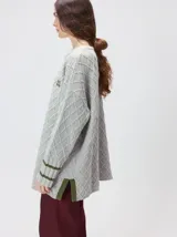 Sweater gris de punto con diseño de rombos, cuello redondo y mangas largas. Cuenta con puños largos acanalados con rayas horizontales en color verde militar y un pequeño logo bordado en el pecho.