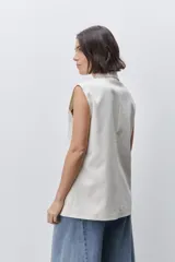 Chaleco sastrero color blanco, de corte amplio y sin mangas, con cuello de solapas y bolsillos delanteros.