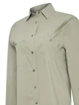 Blusa de manga larga con cuello camisero, confeccionada en una mezcla de algodón orgánico, nylon y spandex. Presenta cierre frontal con botones, dos bolsillos frontales con solapa y paneles laterales con detalle de frunces. Cuenta con tecnología de protección solar UPF.