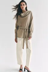 Camisa de cuello fluido y manga larga con puños anchos, de corte recto y largo medio, confeccionada en tejido rústico en tono beige con sutil textura jaspeada. Cuenta con un cinturón ajustable del mismo género para entallar la cintura.