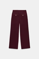 Pantalón de tiro alto color bordó, con pinzas delanteras, bolsillos frontales y falsos bolsillos con solapa en la espalda. Tiene pernera ancha y cierre frontal con cremallera, botón interior y gancho.