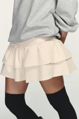 Vestido corto que combina una parte superior tipo sudadera gris de manga larga con puños, y una falda corta de volantes color crema. La parte superior es de tejido de punto jaspeado y la falda tiene dos capas de volantes.