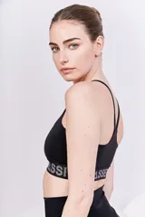 Top deportivo negro con breteles finos y elástico inferior con la marca Bassi estampada en gris. Diseño de espalda cruzada que brinda soporte y sujeción.