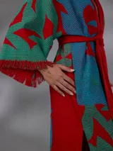 Kimono largo de algodón texturado con estampado vegetal en tonos rojo, azul y verde. Cuenta con mangas amplias, cinto independiente para ajustar a la cintura, bolsillos laterales y aberturas laterales en el dobladillo con detalles de flecos.