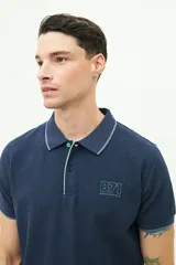 Polo de manga corta Brooksfield en color azul marino con textura. Presenta cuello clásico con cierre de botones, logo estampado en el pecho y detalles en contraste en el borde del cuello y las mangas.