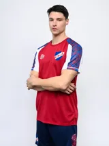 Remera de fútbol Umbro del Club Nacional de Football, modelo Pro Training Active. Diseño con estampado abstracto en blanco, rojo y azul, con mangas raglán azul marino y escudo del club en el pecho.