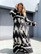 Vestido largo estilo túnica, color negro con estampado ornamental en blanco. Presenta cuello en V con botones y mangas largas amplias.