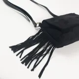 Bandolera negra de gamuza con solapa frontal y flecos laterales largos. Cuenta con herrajes metálicos en tono bronce.