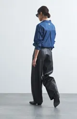 Pantalón de cuero sintético con fit barrel, de silueta amplia con volumen en las piernas y botamanga levemente entallada. Presenta bolsillos laterales y cierre frontal.