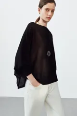 Jersey de punto con diseño tipo capa asimétrica, cuello redondo y mangas largas con puños ajustados.