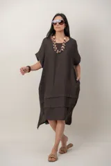 Vestido midi de lino color beige, de corte holgado y silueta acampanada. Cuenta con cuello redondo, mangas cortas amplias, bolsillos laterales y detalles de recortes horizontales en la falda con terminación asimétrica más larga en la parte trasera.