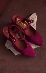 Sandalias de gamuza color fucsia, con punta fina, taco medio y tira ajustable en el empeine. Presentan detalle metálico en la puntera.
