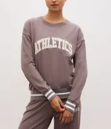 Buzo deportivo de corte oversized color gris topo, con cuello redondo, mangas largas y puños con detalle de rayas blancas. Presenta estampado frontal con la palabra Athletics y ruedo con franja blanca contrastante.