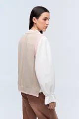 Chaleco de punto color beige con escote en V y ribete blanco.