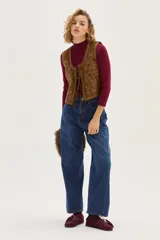 Chaleco de cuero color camel con bordados decorativos, tachas metálicas en los bordes y cierre frontal mediante lazos.