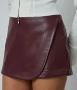Short pollera de tiro alto confeccionado en poliuretano con acabado liso. Presenta un diseño cruzado en el frente, cierre posterior con cremallera y corte ajustado.