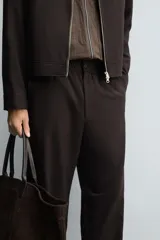 Pantalón regular fit color marrón oscuro, confeccionado en tejido con viscosa. Cuenta con cintura elástica, bolsillos delanteros y detalle de bolsillos traseros de vivo. El cierre frontal es con cremallera y botón.