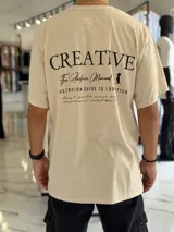 Remera oversize color beige, con diseño estampado en la espalda que incluye tipografía grande y texto descriptivo en negro.