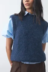 Chaleco de punto con textura afelpada, cuello redondo y hombros marcados. Presenta una silueta relajada y un diseño sin mangas.