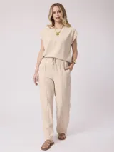 Pantalón fluido de color beige, con cintura elástica con cordón de ajuste y costuras frontales a lo largo de las piernas.
