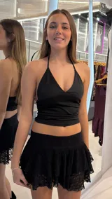 Top halter negro con diseño cruzado en el frente y fruncidos laterales, de corte corto y tirantes ajustables al cuello.