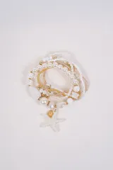 Set de pulseras elásticas con cuentas de perlas, mostacillas doradas y blancas, con dije central de estrella de mar blanca y detalle de caracol dorado.