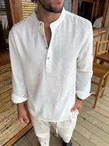 Camisola de cuello mao en color blanco, confeccionada en tela liviana con textura. Presenta cierre frontal parcial con botones de madera y mangas largas con opción de arremangar mediante trabilla.