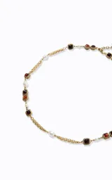 Collar largo de estilo sofisticado con cadena de metal en acabado dorado. Presenta un diseño intercalado con perlas sintéticas y detalles geométricos cuadrados con piedras en tonos rojizos y marrones.