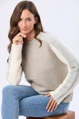 Buzo tejido de abrigo con cuello redondo y manga larga. Presenta un diseño de bloques de color en tonos gris claro y beige.