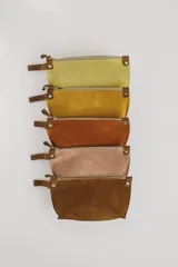 Sobre de mano confeccionado en cuero agamuzado con cierre metálico superior y correa lateral pequeña. Presenta un diseño minimalista con detalles de remaches metálicos en los extremos del cierre.