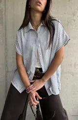 Camisa de manga corta con diseño a rayas celestes y blancas, cuello clásico y cierre frontal de botones.