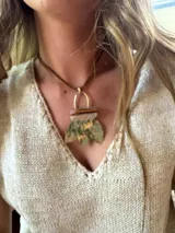 Collar con cordón de cuero marrón y dije con forma de hojas verdes, piezas de madera y aro dorado.