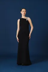 Vestido largo negro de corte sirena y silueta ajustada, con detalle de aplique floral brillante en el hombro izquierdo.