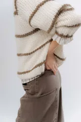 Buzo de tejido de punto grueso en color gris con rayas horizontales en color crema, de corte holgado, cuello redondo y mangas largas.