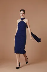 Vestido midi de crepe elastizado color rojo, con escote halter, detalle metálico en el cuello y lazo largo que cae desde el hombro. Diseño ajustado al cuerpo con frunces laterales.